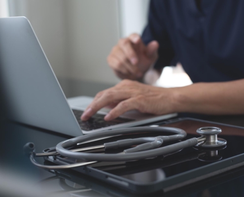Close-up of a healthcare professional working on a laptop with a stethoscope in the foreground